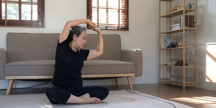 Healthy and happy 60s retired Asian woman in workout clothes practicing yoga in her living room...