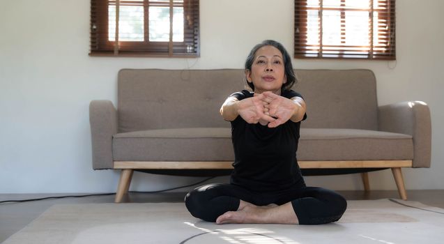 Healthy and happy 60s retired Asian woman in workout clothes practicing yoga in her living room...