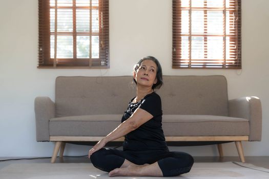 Healthy and happy 60s retired Asian woman in workout clothes practicing yoga in her living room...