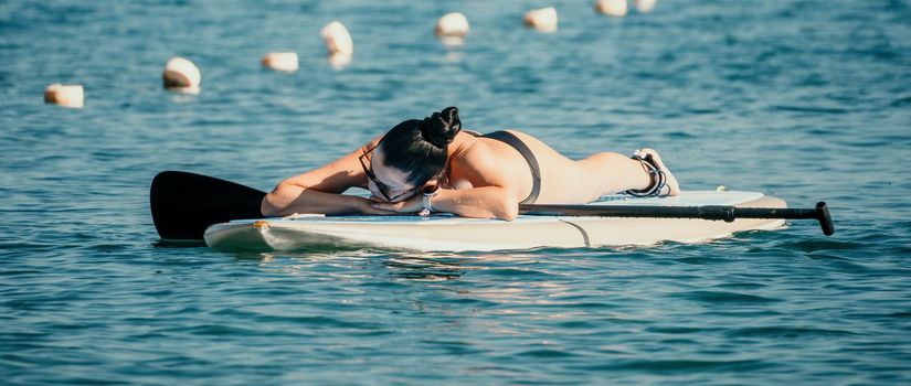 Sea woman sup. Silhouette of happy middle aged woman in rainbow bikini, surfing on SUP board, confident paddling through water surface. Idyllic sunset. Active lifestyle at sea or river