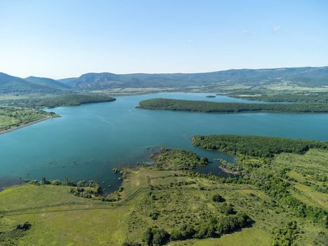 Aerial landscape from flying drone storage reservoir at mountain foot covered colorful spring forest. Beautiful view from above blue lake among highlands