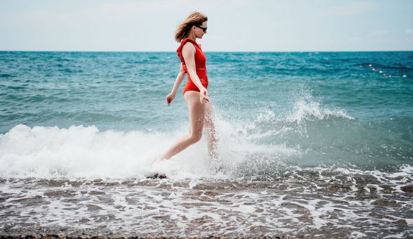 Young happy woman walks carefree on the seaside. Happy lady in red bikini. Portrait beautiful young woman relax smile around beach sea ocean in holiday vacation travel trip.