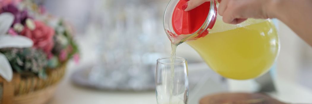 Woman hand pours juice or lemonade from jug into glass. Refreshing vitamin fresh with juice concept