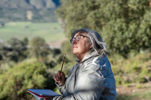 white-haired woman with glasses taking notes in her notebook in the park on a sunny winter's day