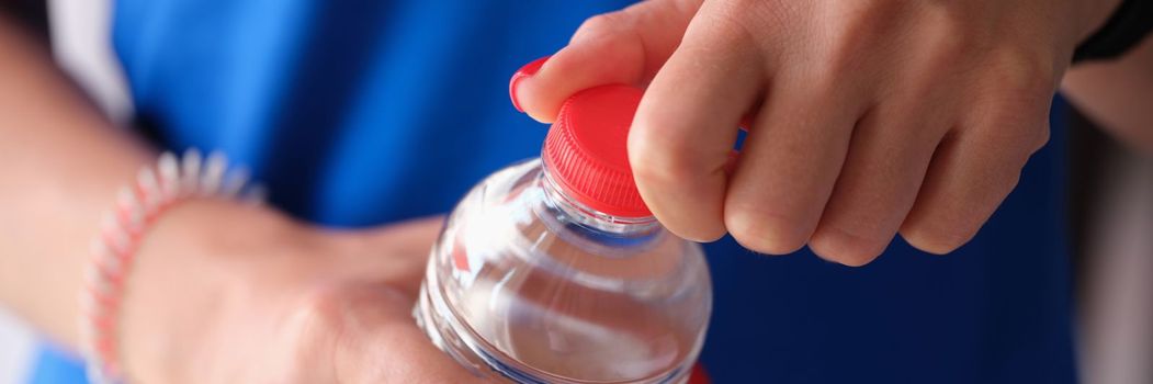 Woman opens plastic red cap of water bottle. Choice of drinking water concept