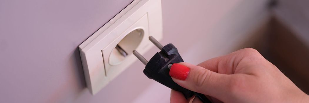 Connecting black electric plug with hand to white plastic socket on awhite wall. Connecting household appliances