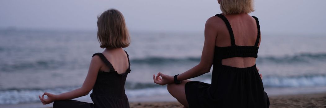 Mom and daughter do yoga and meditate on beach. Family meditation by the sea relaxation and tranquility concept