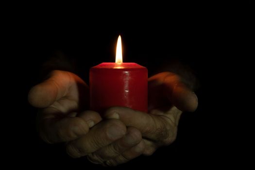 man holding a red candle with both hands, black background and copy space