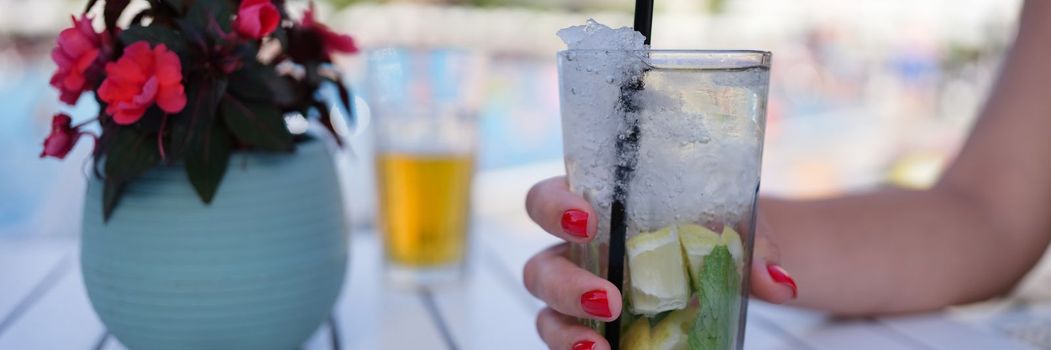 Glass with lemonade lemon slices and ice cubes in female hand. Summer cold refreshing drink concept