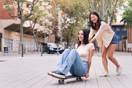 two young women have fun playing with a skateboard in the street, concept of friendship and teenager lifestyle, copy space for text