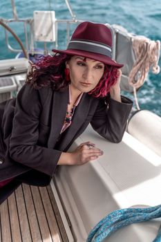 Portrait of a woman on a yacht in the sea, she has burgundy curly hair, looks to the side