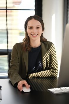 Portrait of caucasian female manager in elegant suit sitting at her workplace and smiling to camera.