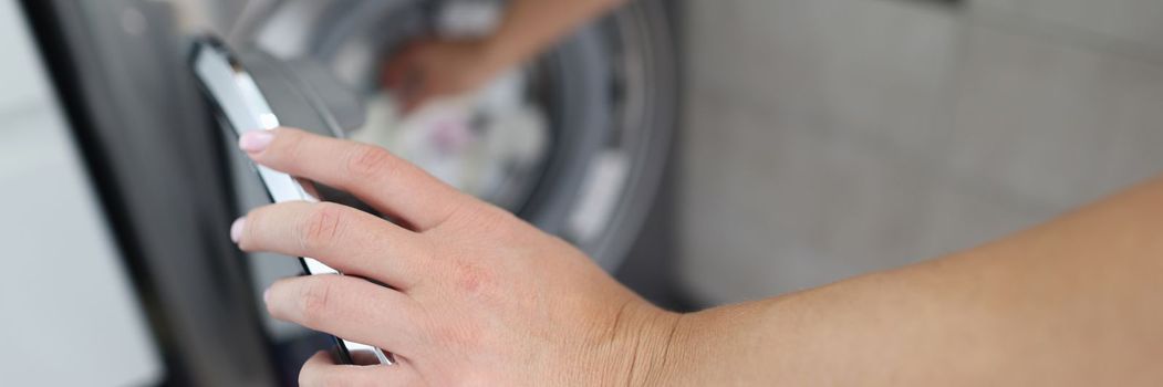 Woman hand fills drum of washing machine. Household chores and turning on washing machine concept