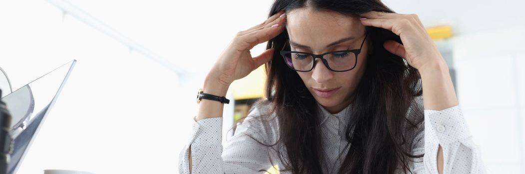 Tired sleepy woman sits at table holds head and rests at the workplace. Bored young woman feeling sleepy lazy and unmotivated at work