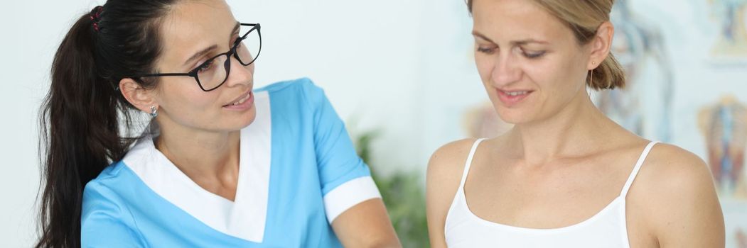 Female patient receiving medical care in rehabilitation center after leg injury. Physiotherapist examining leg and knee of woman sitting on medical couch