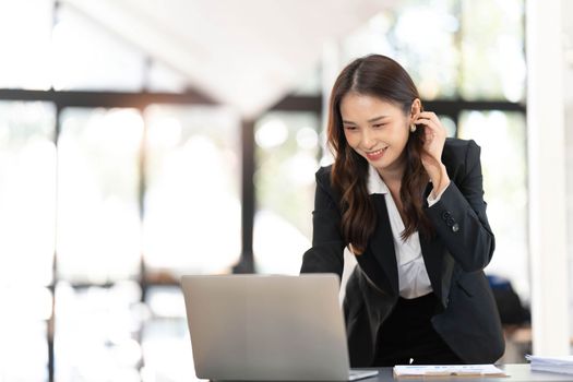 Focused young businesswoman standing at table in office, using laptop, looking at computer screen, reading or writing business email, searching information in internet, working on project..