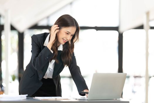 Focused young businesswoman standing at table in office, using laptop, looking at computer screen, reading or writing business email, searching information in internet, working on project..