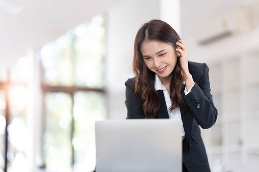 Focused young businesswoman standing at table in office, using laptop, looking at computer screen, reading or writing business email, searching information in internet, working on project..