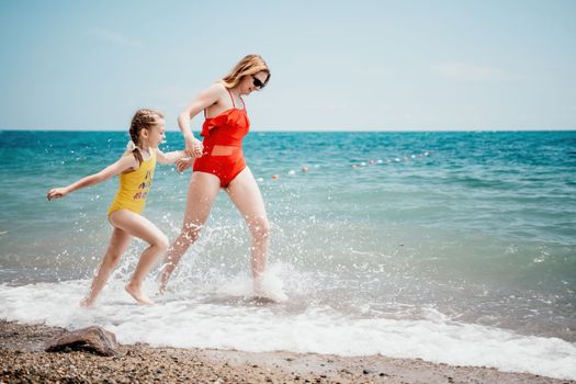 Happy loving family mother and daughter having fun together on the beach. Mum playing with her kid in holiday vacation next to the ocean - Family lifestyle and love concept.