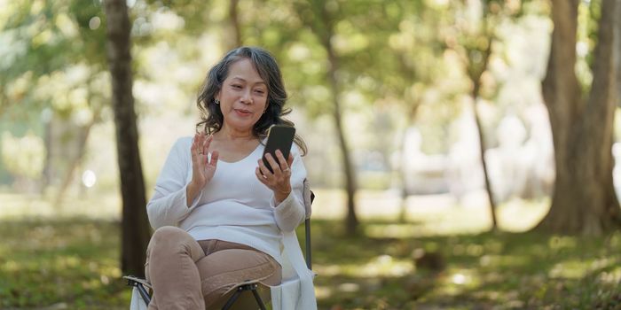 Happy senior asian woman at outdoor park and talking on video call with family.