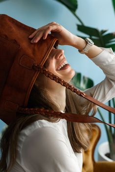close-up photo of orange leather bag on a womans had. indoor photo. beautiful girl in a white blouse having fun with a handbag