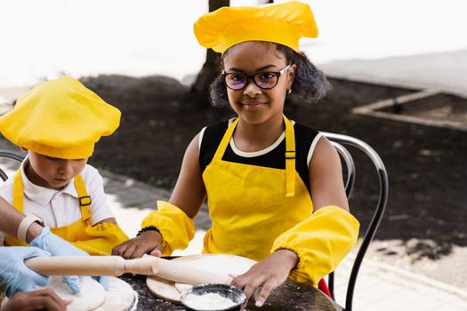 Multinational company of children cooks in yellow uniforms cooking dough for bakery. African teenager and black girl have fun with caucasian child boy and cook food