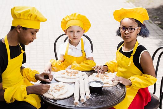 Happy company of multiethnic children cooking dough. Childhood cook activity of multinational children of black african and caucasian kids