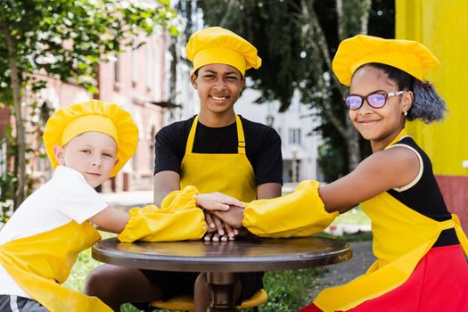 Multiracial children cook touching hands together forming pile. Friendship of multinational kids. Childhood. cooks in chefs hat and yellow apron uniform put hands on each other