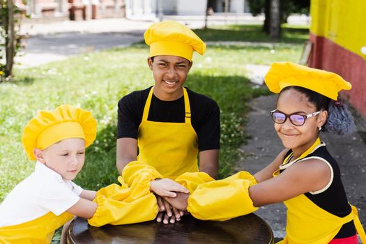 Multiracial children cook touching hands together forming pile. Friendship of multinational kids. Childhood. cooks in chefs hat and yellow apron uniform put hands on each other