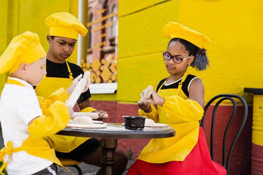 Childhood cook activity of multinational children of black african and caucasian kids. Happy company of multiethnic children cooking dough