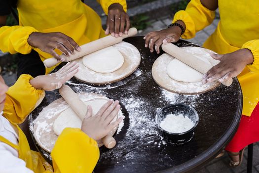 Multiracial hands of children cooks cooking and rolling dough close-up. Young cooks children cooking khachapuri