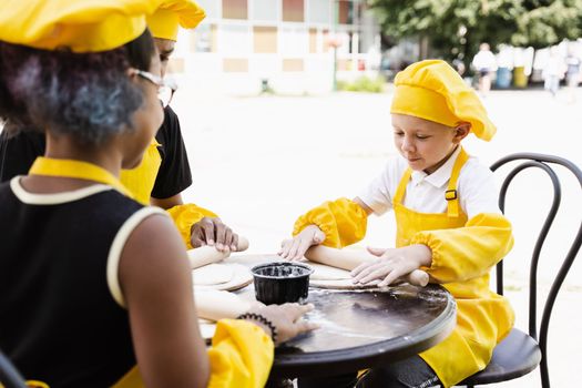 Handsome cook child in yellow chefs hat and apron yellow uniform rolling dough and cooking outdoor