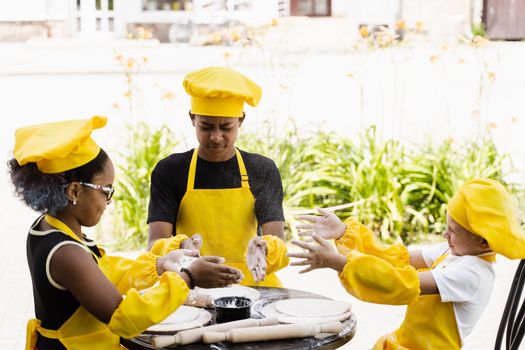 Multiracial children cooks play with flour for dough and having fun. Multinational cook kids in chefs hat and yellow apron uniform cooking outdoor for bakery