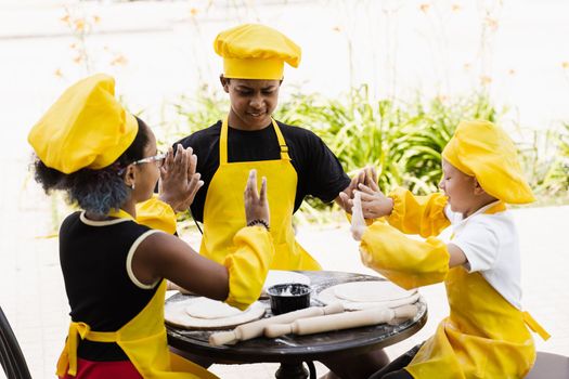 Multiracial children cooks play with flour for dough and having fun. Multinational cook kids in chefs hat and yellow apron uniform cooking outdoor for bakery