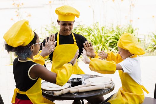 Multiracial children cooks play with flour for dough and having fun. Multinational cook kids in chefs hat and yellow apron uniform cooking outdoor for bakery