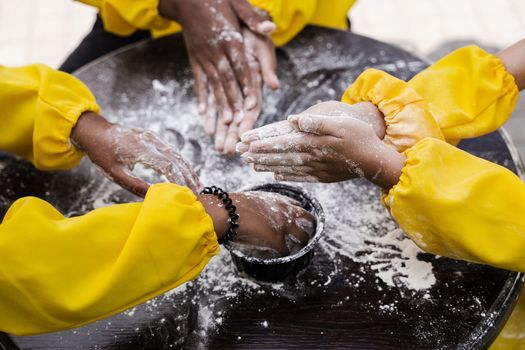 Hands of multinational children cooks play with flour for dough and having fun close-up. Young cooks children cooking khachapuri.