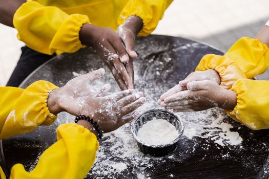 Hands of multinational children cooks play with flour for dough and having fun close-up. Young cooks children cooking khachapuri.