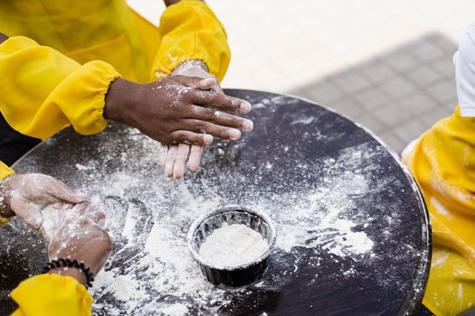 Hands of multinational children cooks play with flour for dough and having fun close-up. Young cooks children cooking khachapuri.