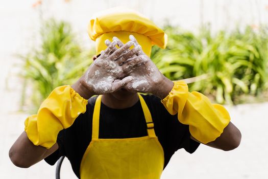 Black african cook teenager showing hands with flour and close his face. African child in chefs hat and yellow apron uniform