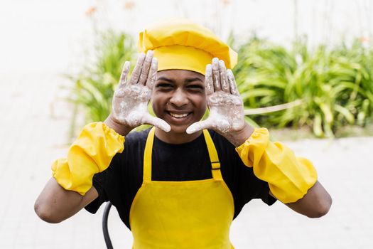 Black african cook teenager showing hands with flour and smiling. African child in chefs hat and yellow apron uniform