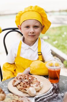 Attractive cook child boy in chefs hat and yellow apron uniform with khachapuri and summer lemonade