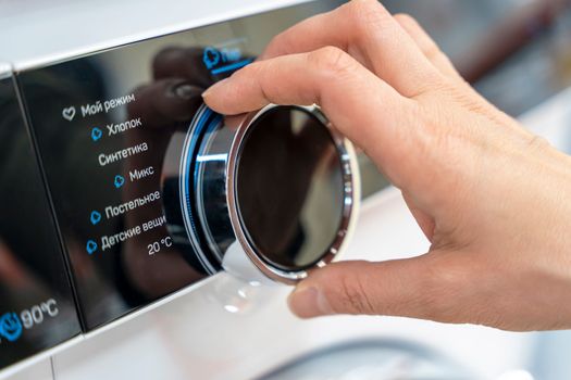 a woman's hand selects the washing mode with a round selector on the control panel of a modern washing machine. technologies. close-up. choosing a washing program
