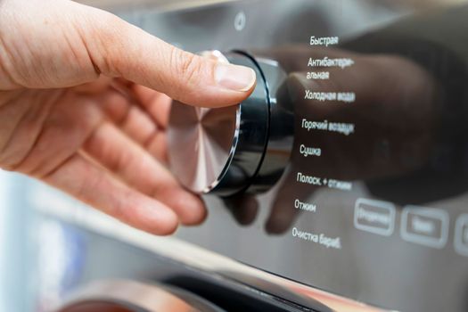 a woman's hand selects the washing mode with a round selector on the control panel of a modern washing machine. technologies. close-up. choosing a washing program