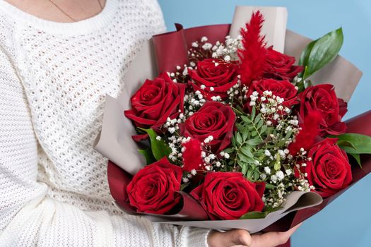 a beautiful bouquet of fresh red roses in women's hands on a light blue background. Congratulations on Mother's Day. valentine's day. wedding