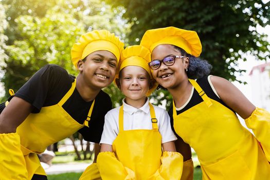 Multiracial company of children cooks in yellow uniforms smile outdoor. African teenager and black girl have fun with caucasian child boy and cook food. Kids portrait