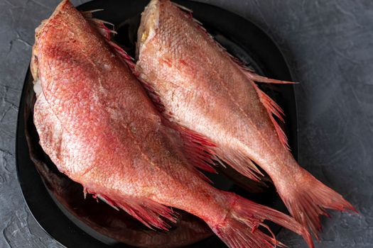 Two frozen headless carcasses of red sea bass, covered with frost on a plate. Kitchen. Fish diet