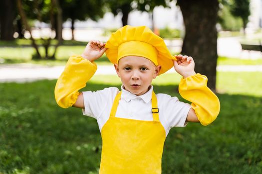 Shocked cook child in yellow chefs hat and apron yellow uniform holding chefs hat and surprise outdoor