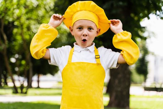 Shocked cook child in yellow chefs hat and apron yellow uniform holding chefs hat and surprise outdoor