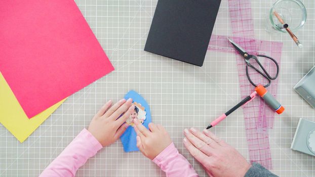 Flat lay. Little girl making a handmade Father's Day card from construction paper.