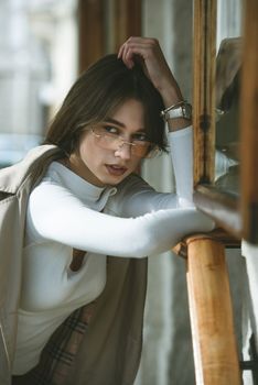 beautiful brunette girl in a sunglasses dressed in white blouse and beige coat. Stylish trendy fashion outlook.